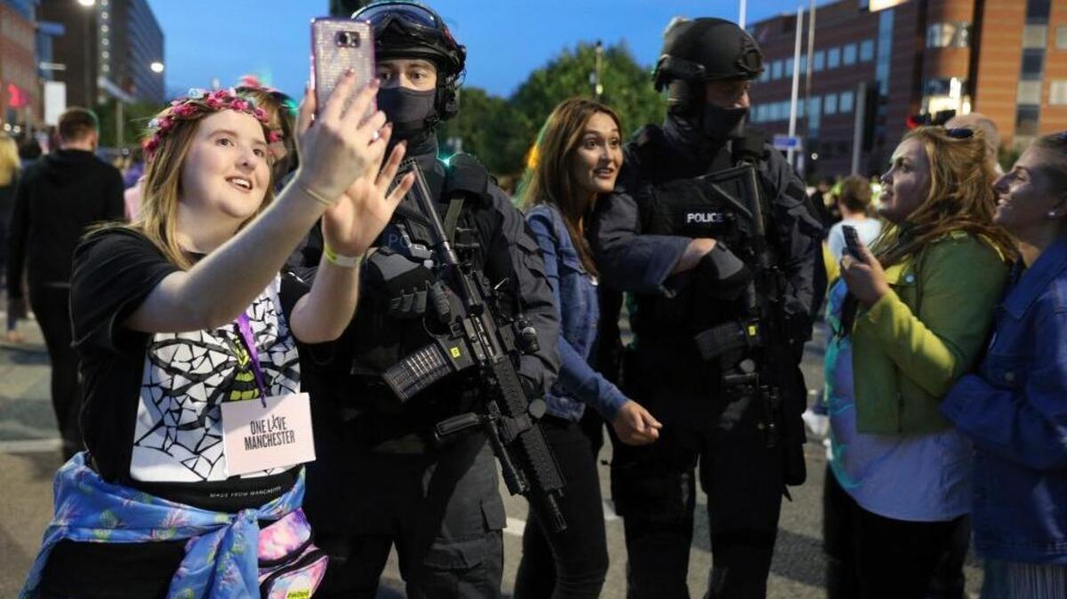 Concert-goers take selfies next to armed police as they depart the One Love Manchester concert on Sunday in Manchester, England. Ariana Grande returned to the city to pay tribute with an energetic, all-star concert two weeks after a suicide bombing killed 22 people and injured dozens.