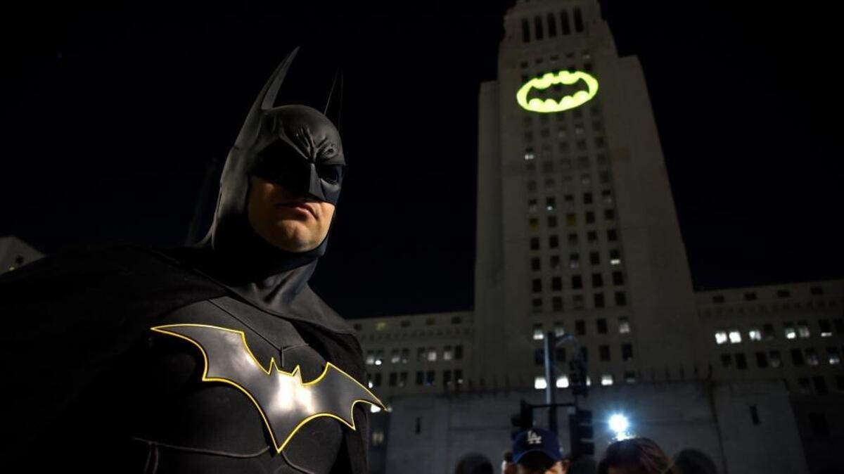Tony Bradshaw, dressed as Batman, poses in front of a Bat-Signal projected onto City Hall during a tribute to “Batman” star Adam West on Thursday in Los Angeles.