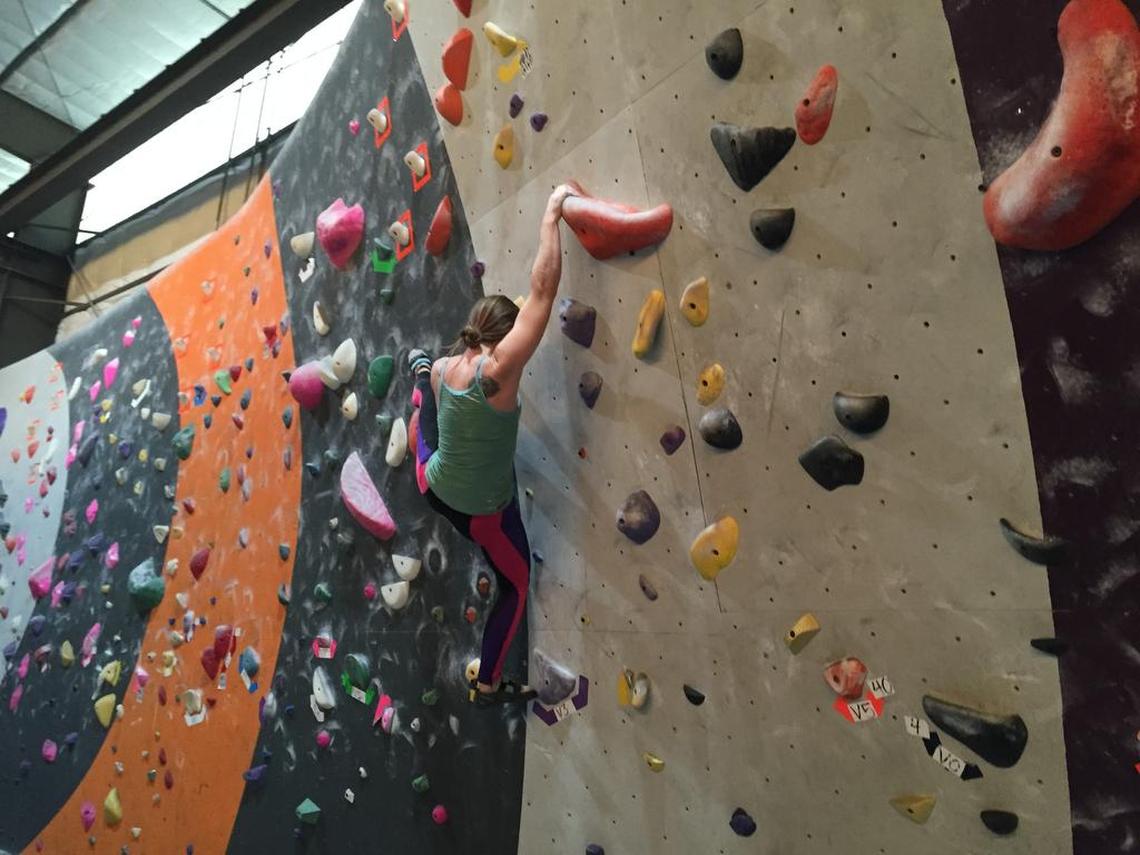 A climber navigates the bouldering wall at Sacramento Pipeworks Climbing and Fitness. The 17-foot walls contain “routes” marked with colorful hand-holds.