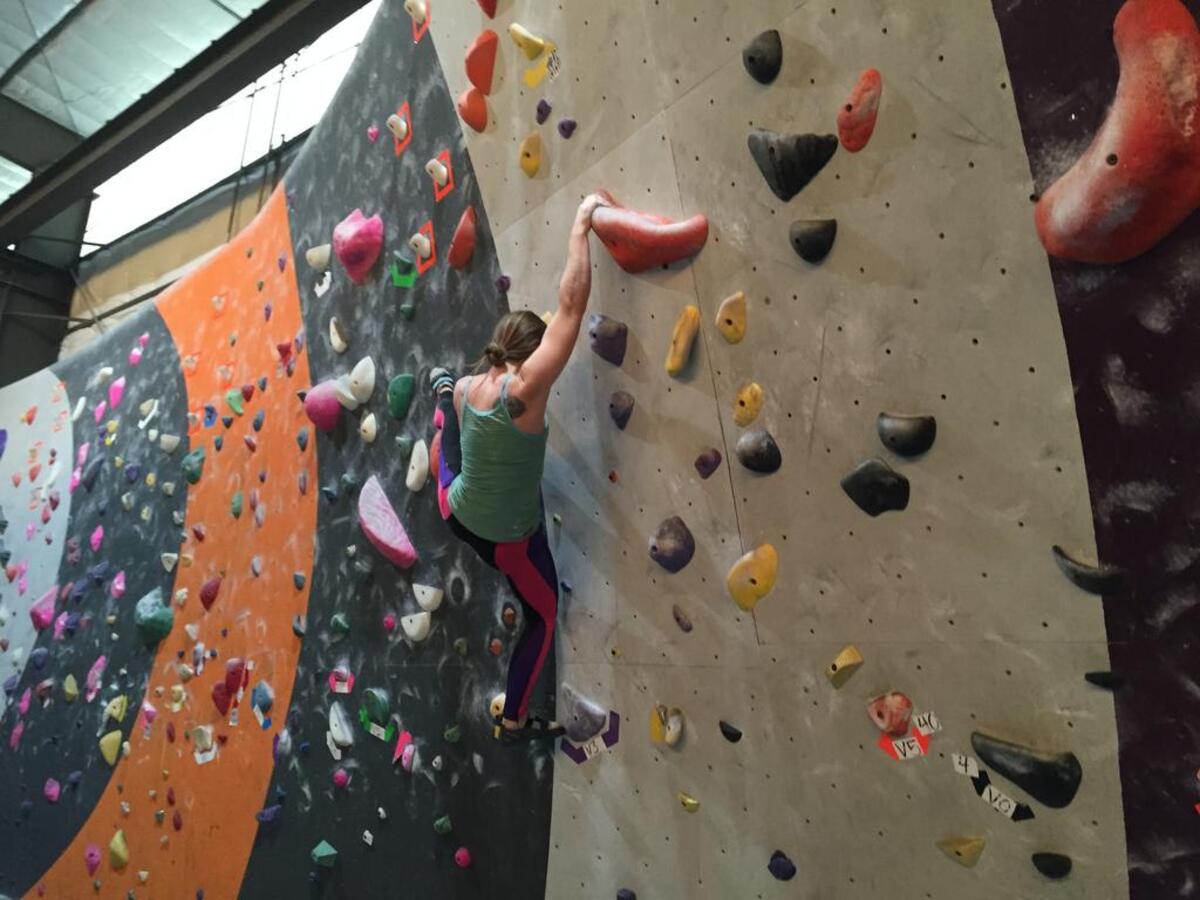 A climber navigates the bouldering wall at Sacramento Pipeworks Climbing and Fitness. The 17-foot walls contain “routes” marked with colorful hand-holds.