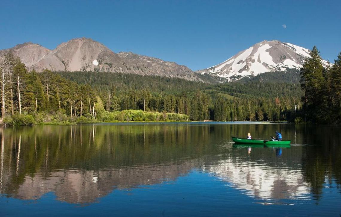 Chaos Crags, top left, and Lassen Peak, with snow at right, loom over the occupants of a canoe on Manzanita Lake in Lassen Volcanic National Park on July 7, 2006.