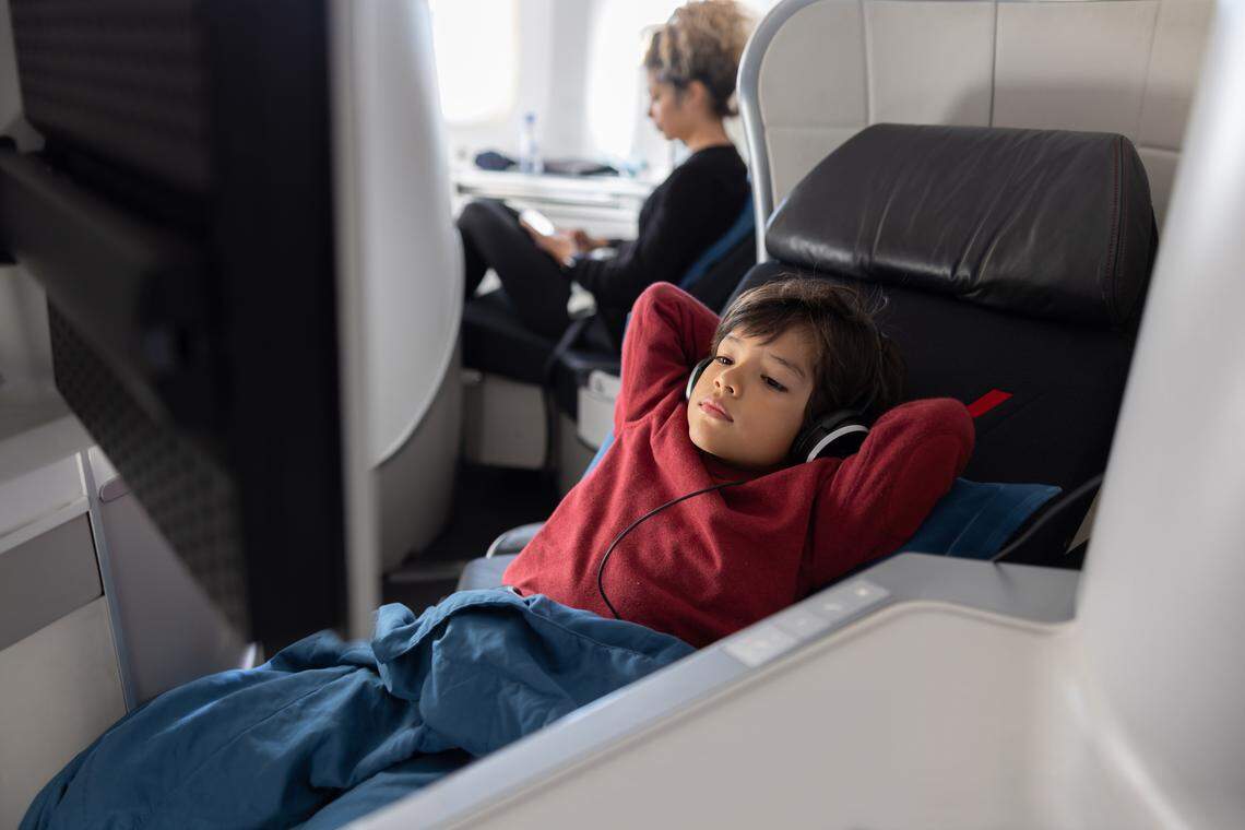 A young boy boy traveling by plane in business class and watching a movie using headphones.