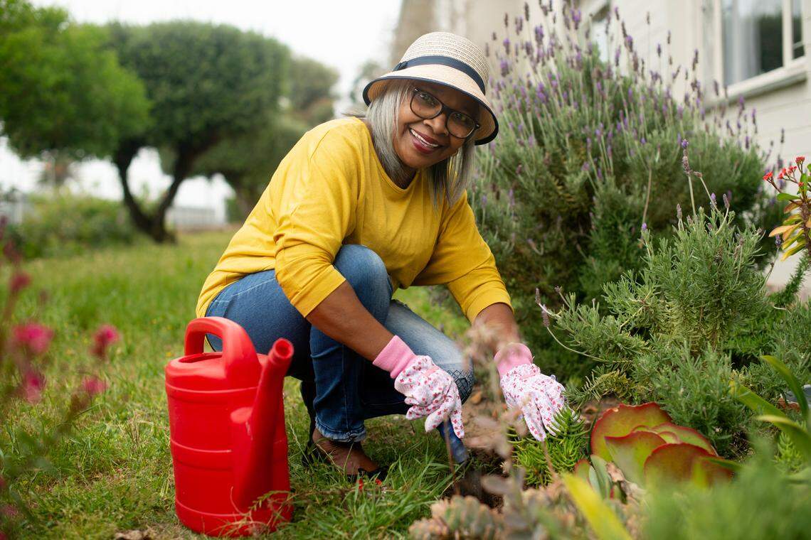 A senior woman smiling while working outside in her garden.