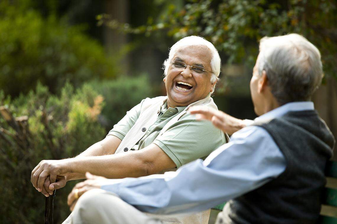 Two retired elderly men sitting on a park bench chatting.