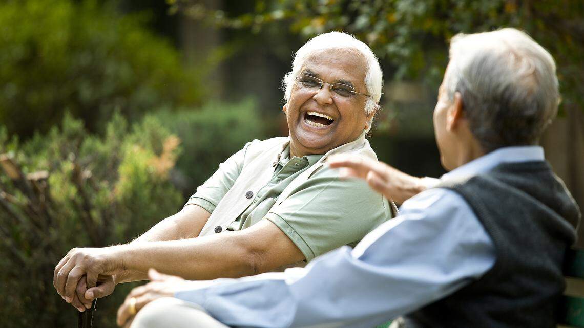 Two retired elderly men sitting on a park bench chatting.