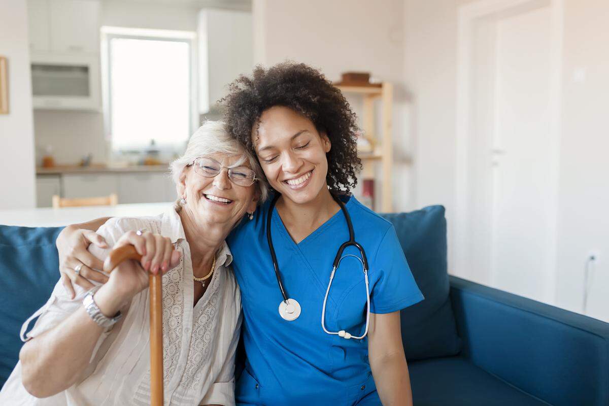 A smiling senior woman with a nurse visitng her home.