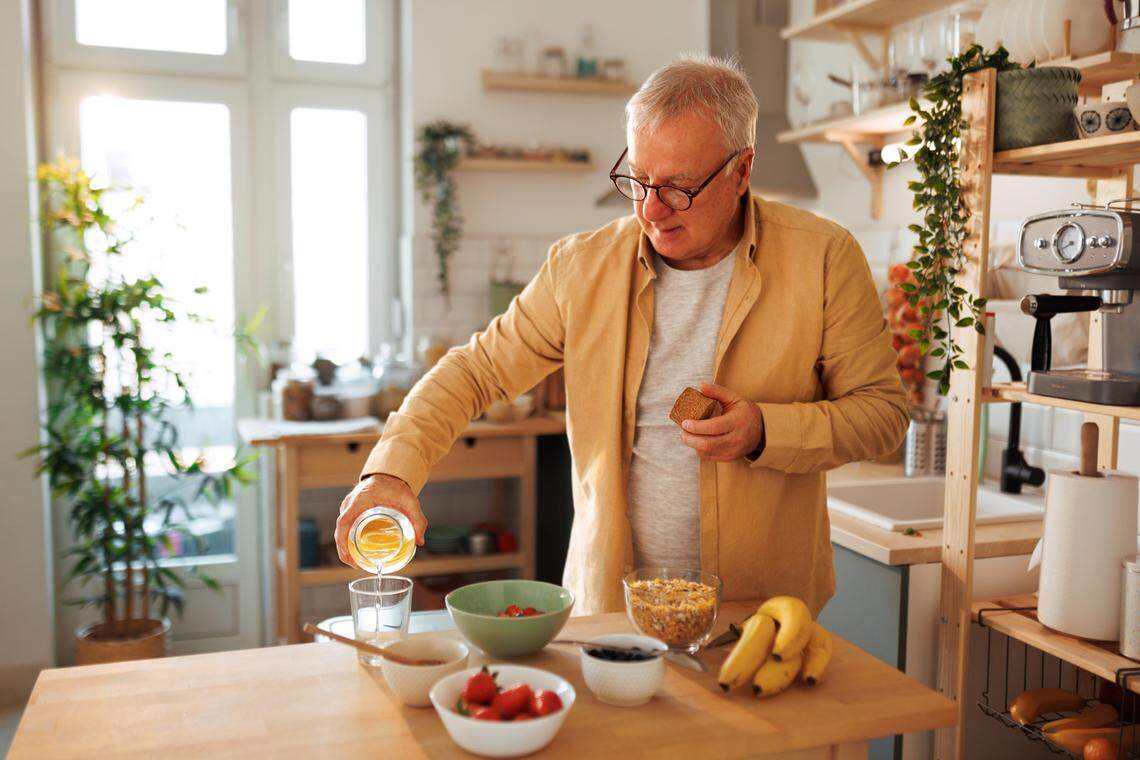 Senior man pouring water in glass while having breakfast in his kitchen.