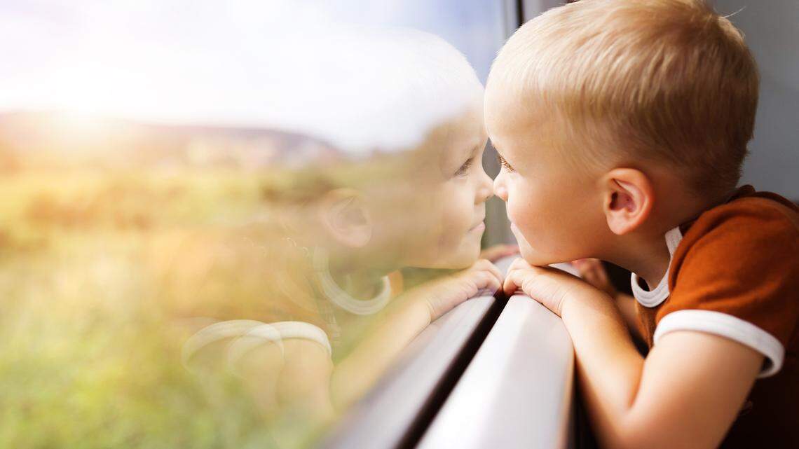 Little boy traveling in train looking outside the window.