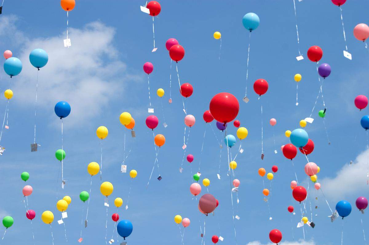Many balloons with notes attached floating up into the sky.