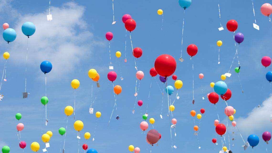 Many balloons with notes attached floating up into the sky.