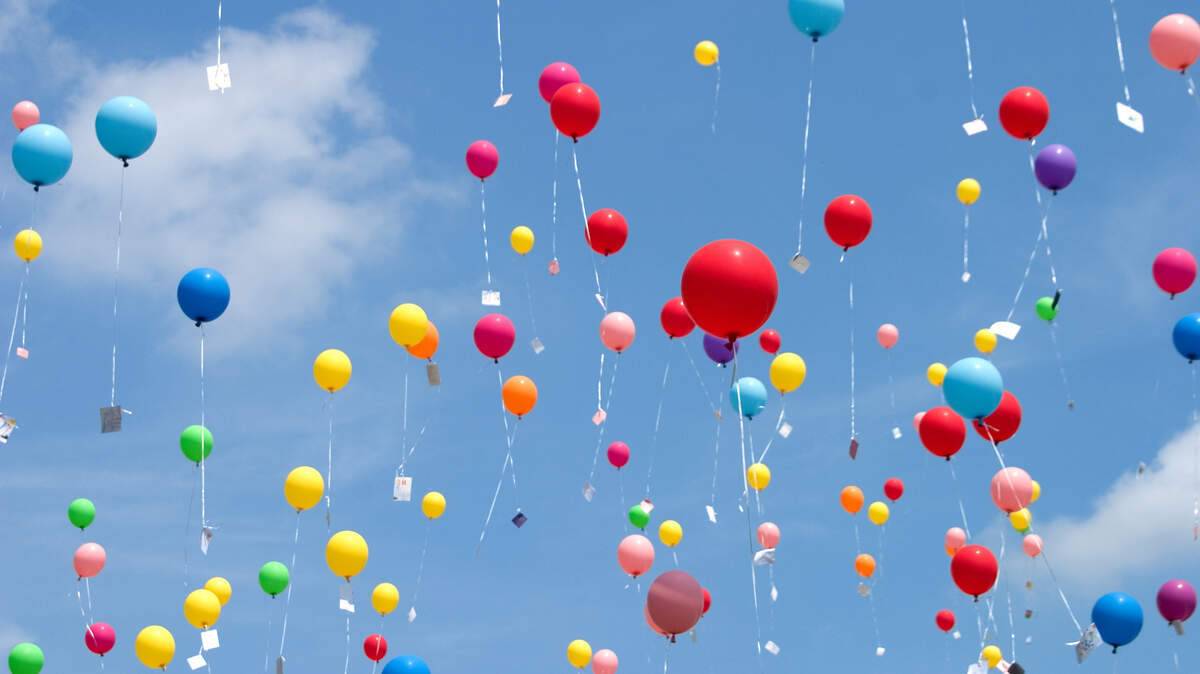 Many balloons with notes attached floating up into the sky.