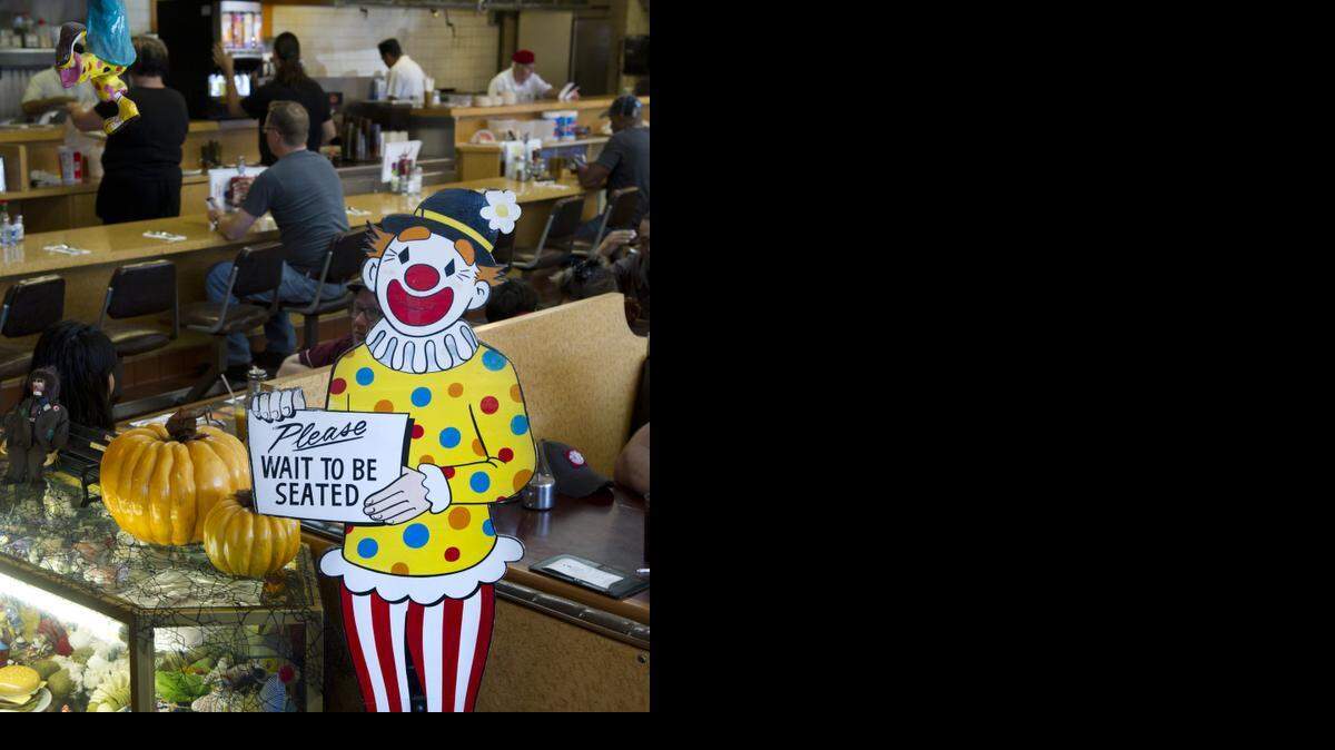 
A wooden cut-out clown holds a sign to wait to be seated in the foyer at Pancake Circus, which has an extensive collection of clown artworks donated by customers.
