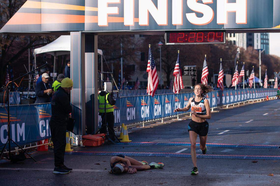 Lauren Hurley, second woman to finish, lies on the ground as Elaina Tabb, third woman to finish, crosses the finish line in the 2022 California International Marathon from Folsom to the state Capitol in downtown Sacramento on Sunday.