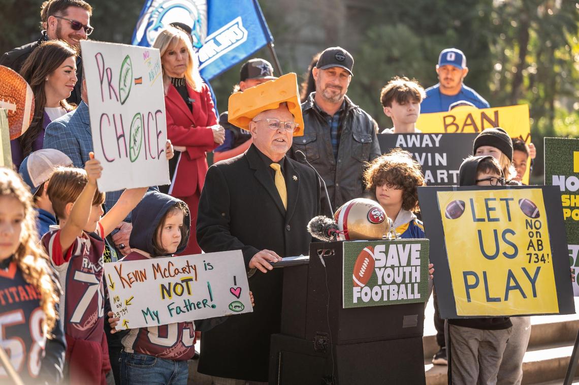Assemblyman Tom Lackey, R-Palmdale, wears a cheesehead hat as he expresses his opposition Wednesday to a bill that would limit youth tackle football at a rally with parents and kids at the state Capitol. Gov. Gavin Newsom has threatened to veto Assembly Bill 734 if it passes the Legislature.
