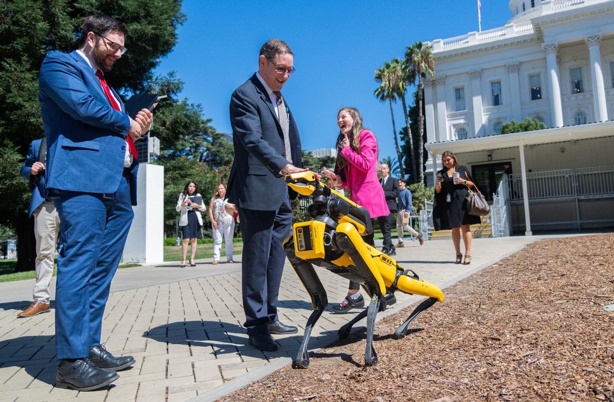 Republican Caucus consultant Daniel Ballon, center, pets Boston Dynamics’ robot dog Spot while caucus floor manager Bryce Pamer, left, and Marissa Forte with the Young Americans for Liberty, back, watch outside the state Capitol on Thursday. The company brought Spot to the state Capitol to support AB 2681, which would prohibit individuals from operating a robotic device or unmanned aircraft that is equipped or mounted with a weapon.