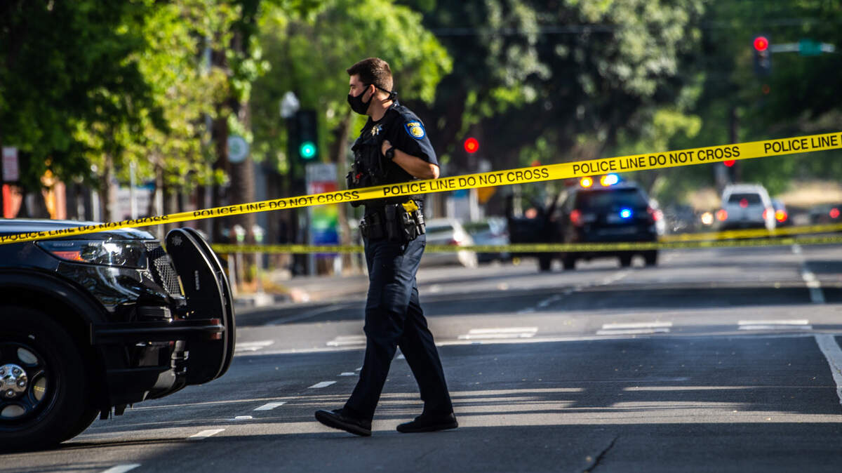 A police officer walks past crime scene tape on 21st and L streets in midtown Sacramento on Thursday, April 22, 2021, following a shooting that killed one man and wounded another early Thursday morning.
