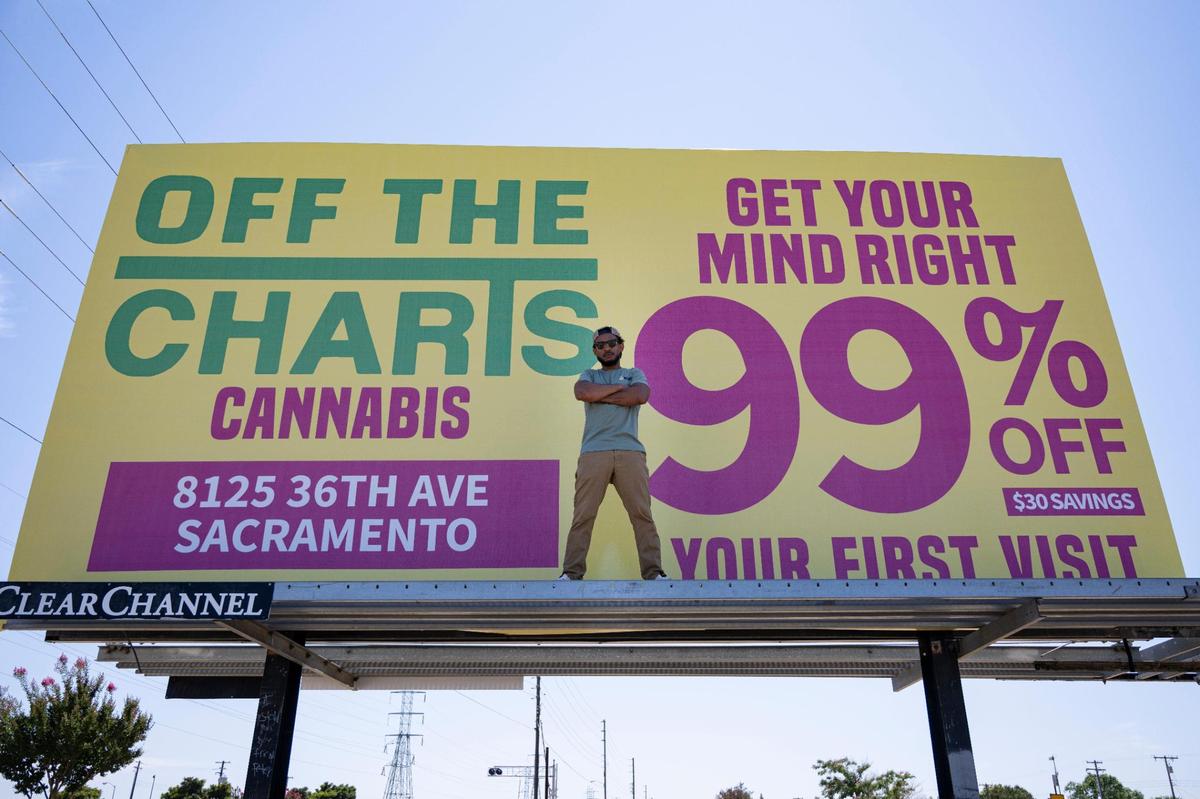 Owner Mike Snell stands on his Off The Charts billboard on Power Inn Road in Sacramento earlier this month.