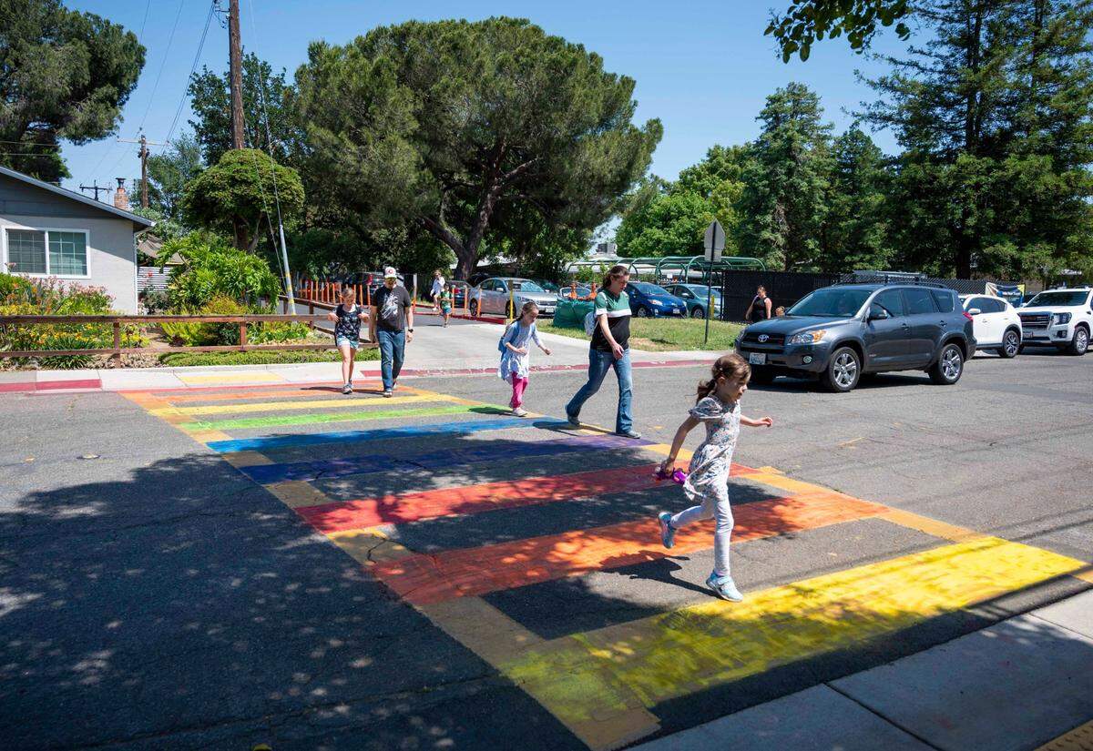 Parents and students cross the street a rainbow-colored crosswalk across from Birch Lane Elementary School in Davis on May 25, 2023.