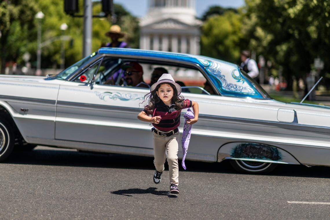 Camila Maciel, 4, runs back to her parents after she had her photo taken in front of a Chevy Impala during the California Lowrider Holiday celebration on Sunday on Capitol Mall.