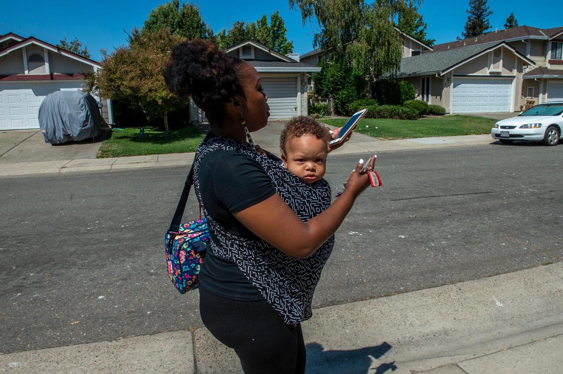 Racquel A. Payton checks information for her second job at DoorDash as she walks her son Yahir, 1, to daycare from her apartment, Tuesday Aug. 20, 2019 in Sacramento. Her job as a preschool teacher begins soon and she worries how she will pay for his full-time child care.