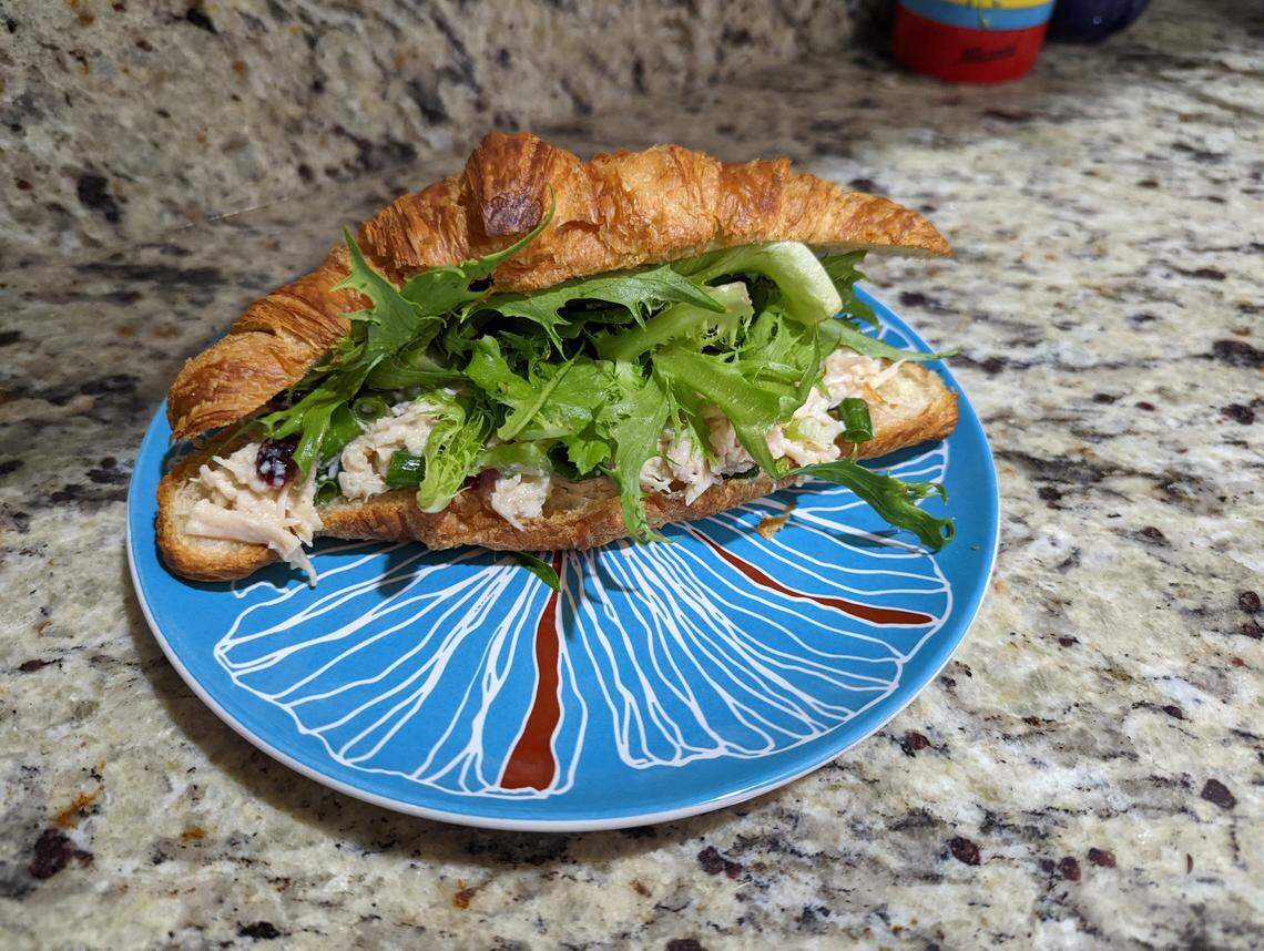 A croissant stuffed with chicken salad and lettuce on a blue plate.
