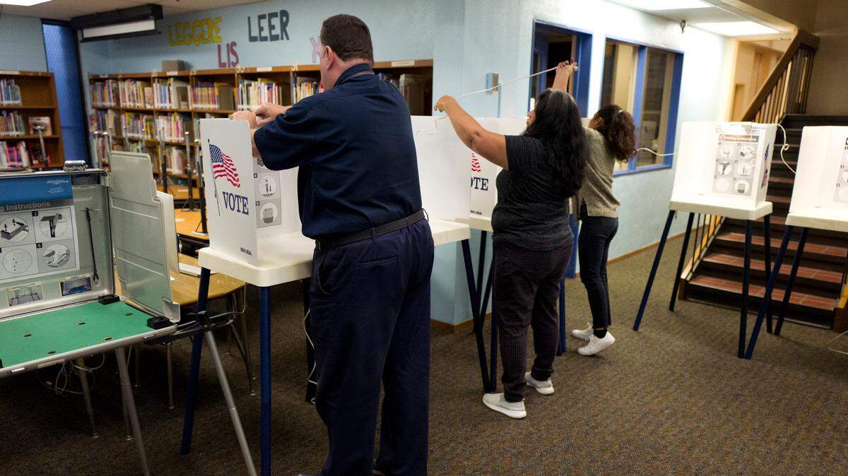 An election worker helps volunteers string lights as they set up voting booths at a polling station inside an elementary school library in Los Angeles on Tuesday. A printing error left more than 118,000 names off the lists at 1,530 precincts, according to the county Registrar-Recorder/County Clerk's Office. Californians statewide are voting in primary elections Tuesday.