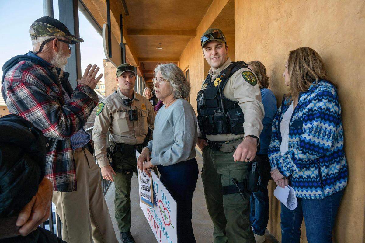 Gina Abrams, center, part of the leadership team for Indivisible El Dorado, holds a sign outside U.S. Rep. Tom McClintock’s office in El Dorado Hills Town Center as a sheriff’s deputy and a private security guard attempt to disburse the group on Friday. McClintock was not there, but groups of seven people were allowed inside the office to speak to a staffer about their concerns with President Trump and Elon Musk.