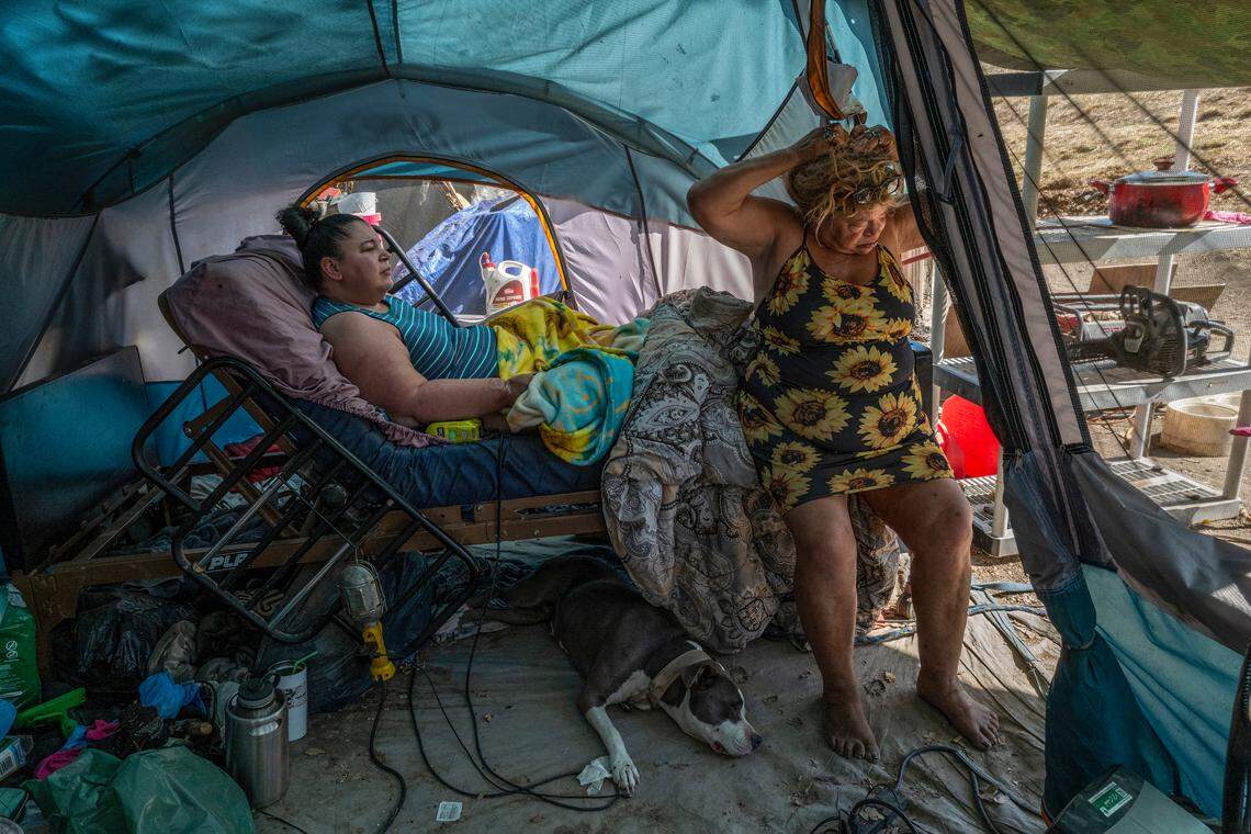Holly Porter lies in her hospital bed while mother Deborah Casillas lifts her hair to catch a breeze in Porter’s tent near the American River in October. On the sweltering hot day, Porter’s dog Felicia rests beneath the bed, which requires a generator to operate. Porter, who suffers from quadriplegia, moved in April to the American River site after she and her mother were swept from the encampment on Colfax Street. Porter moved back to the Colfax site because the river location was susceptible to flooding.