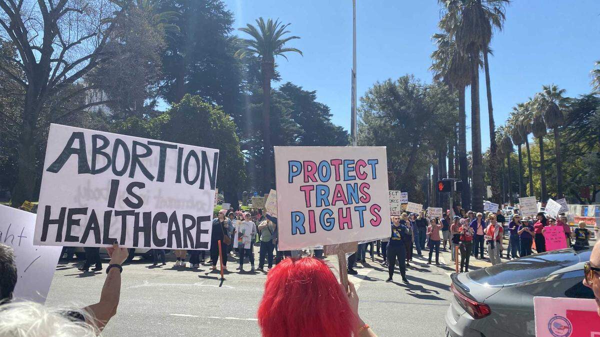 Dawn Pedersen on Saturday March 8, 2025, holds a “Protect Trans Rights” protest sign as she participates in an International Women’s Day demonstration at the corner of L and 10th streets in downtown Sacramento.