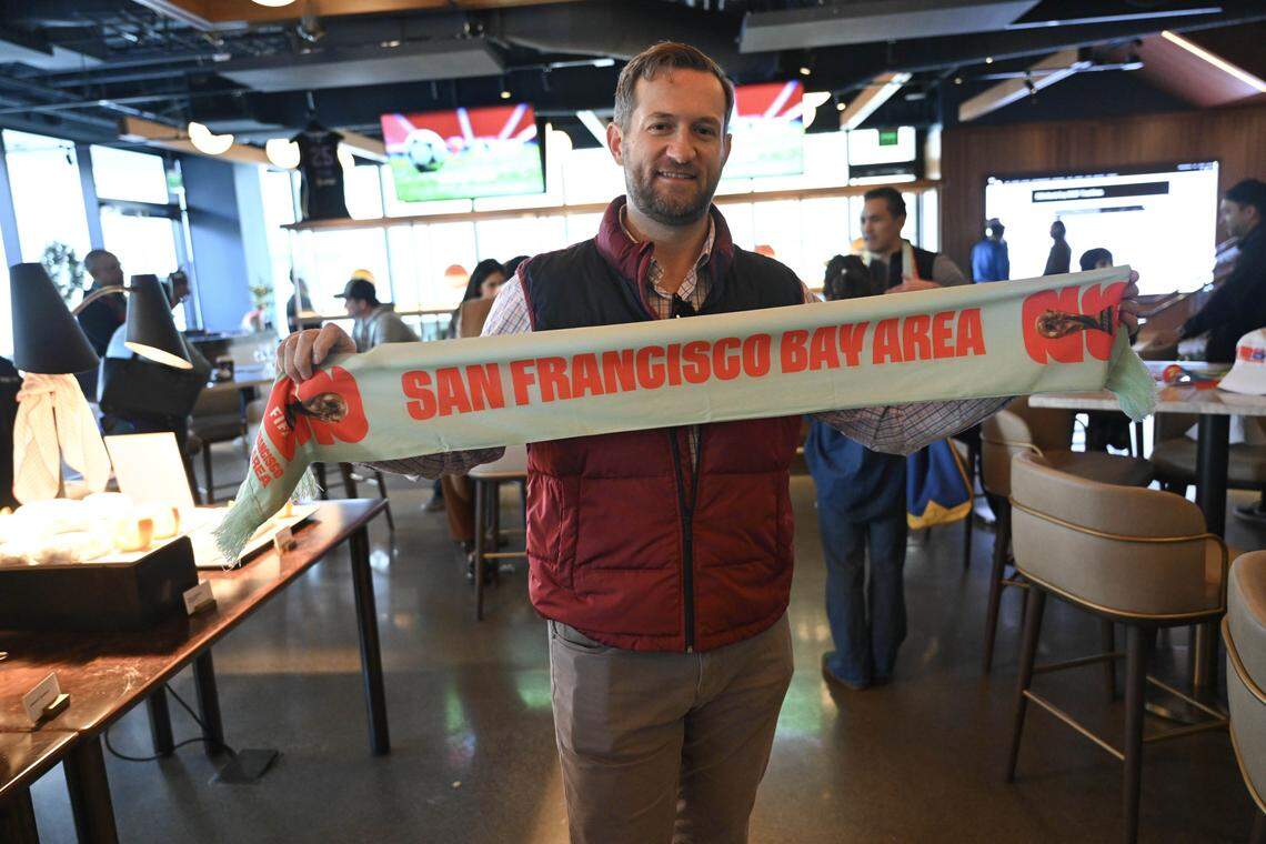 El ex concejal de la ciudad de Sacramento Steve Hansen muestra una pancarta del Área de la Bahía de San Francisco mientras los aficionados al fútbol se reúnen dentro del Splash Sports Bar durante el evento del sorteo del World Cup en Chase Center el viernes 5 de diciembre de 2025.