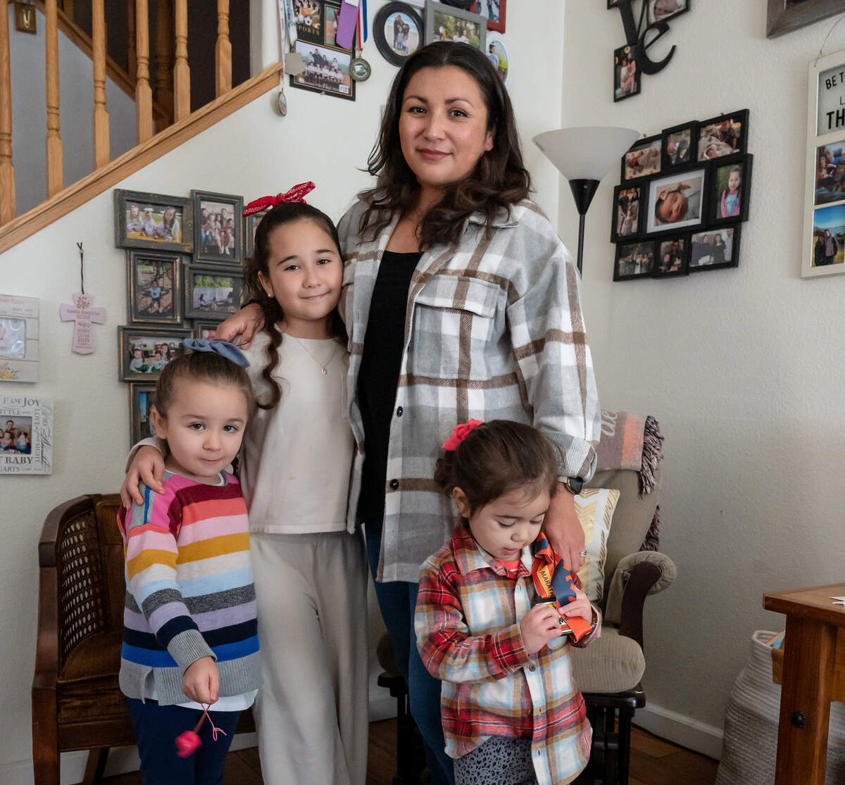 Augustina Kuen, wife of Aaron Kuen, poses for a photo with the couple’s children – Olivia, left, 4; Norah, second to left, 9; and Amelia, right – on Sunday, Jan. 22, 2023, in front of family photos at her home in Elk Grove. Amelia holds her father’s medal from the California International Marathon, where he suffered cardiac arrest.