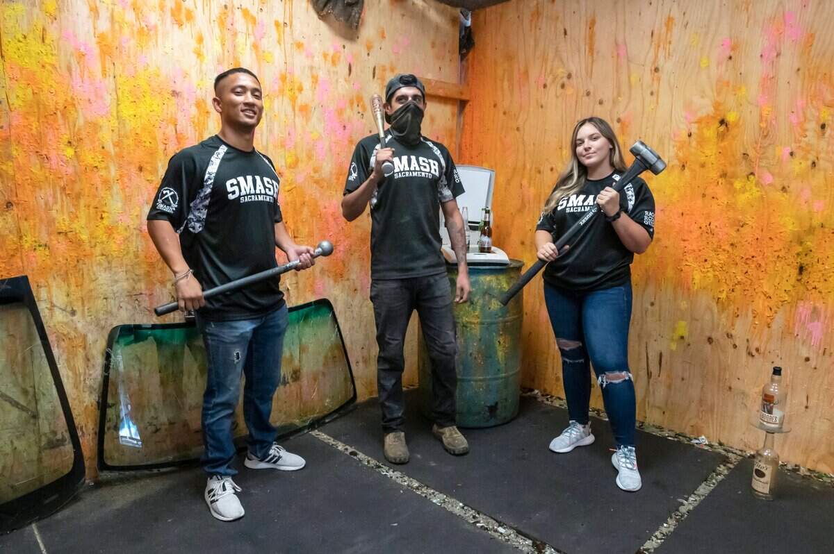 Owner David Messier, left, “rage room” guide Lip Villarreal, center, and manager Breanna Wilkie pose Monday with “weapons” used to destroy things at Smash Sacramento in Carmichael. Messier, an Army veteran, opened the location in 2018 and has since added a second location in downtown Sacramento.