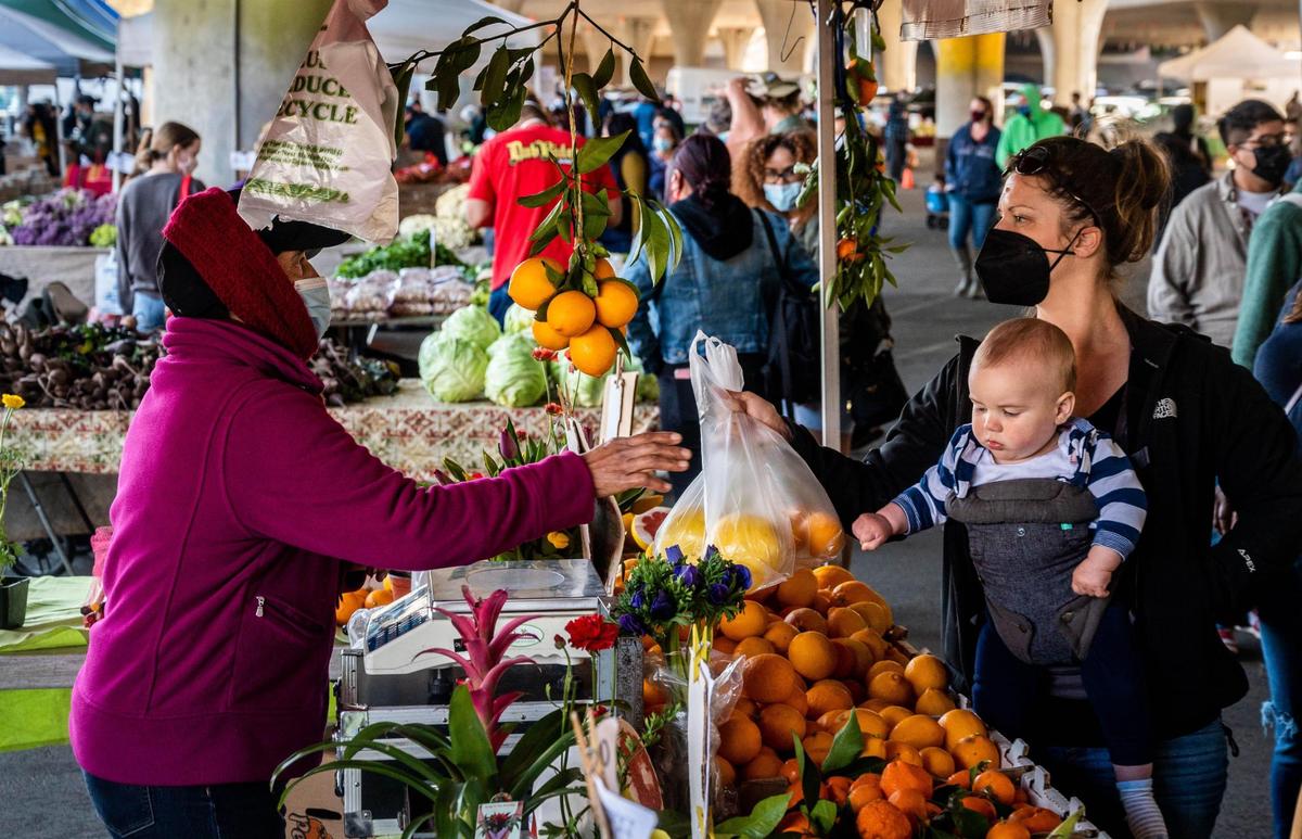 Elizabeth Mailhot and her 10-month-old son Asher buy citrus from a vendor at the Sunday Certified Farmer’s Market near Southside Park on Feb. 28, 2021, the last day before it temporarily moves to Arden Fair mall because of a construction project on the W/X freeway. The market reopens March 21 at the new spot.