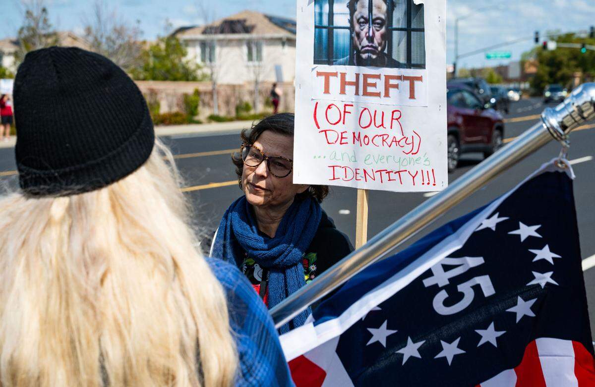 Anti-Tesla demonstrator Christina Rosen, center, and Trump supporter Michaela Swaney, left, carrying a “45” American flag, engage in a civil debate down the street from the Rocklin Tesla dealership on Saturday, March 29, 2025.