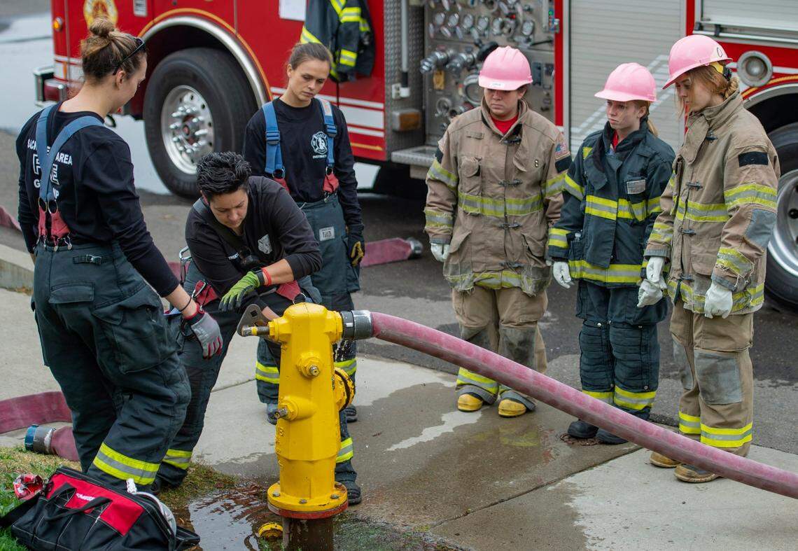 Monica Wilouza, center, of the Sacramento Fire Department, shows the campers how to connect the hose to the fire hydrant at one of the stations at the Sacramento Area Girls Fire Camp at McClellan Park on Saturday, Oct. 23, 2021.