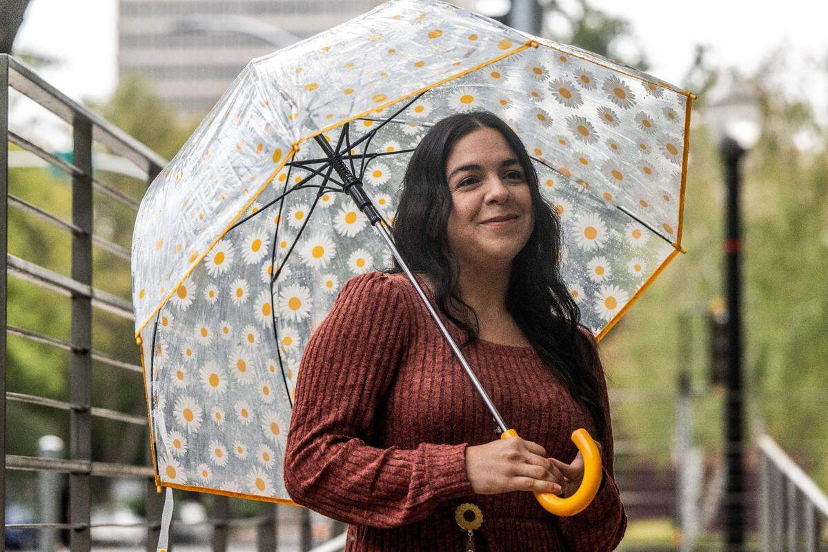 CalPERS employee Sarah Sheppard carries a daisy umbrella stops to talk to a friend as light rain falls in downtown Sacramento on Monday, Sept. 16, 2024.