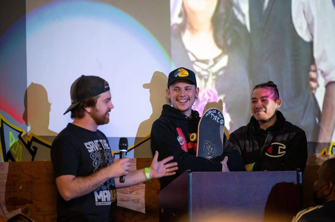 Austin Roberts holds his skateboard with the words “Justice for Tyre” while he and Harry Silva, right, listen to Ryan Wilson reminisce during a memorial and celebration of life for their friend and Sacramento native Tyre Nichols at Sac Ramp Skate Shop on Feb. 4 in Sacramento. Photos projected behind them are of Nichols, who was beaten by Memphis police and died Jan. 10.