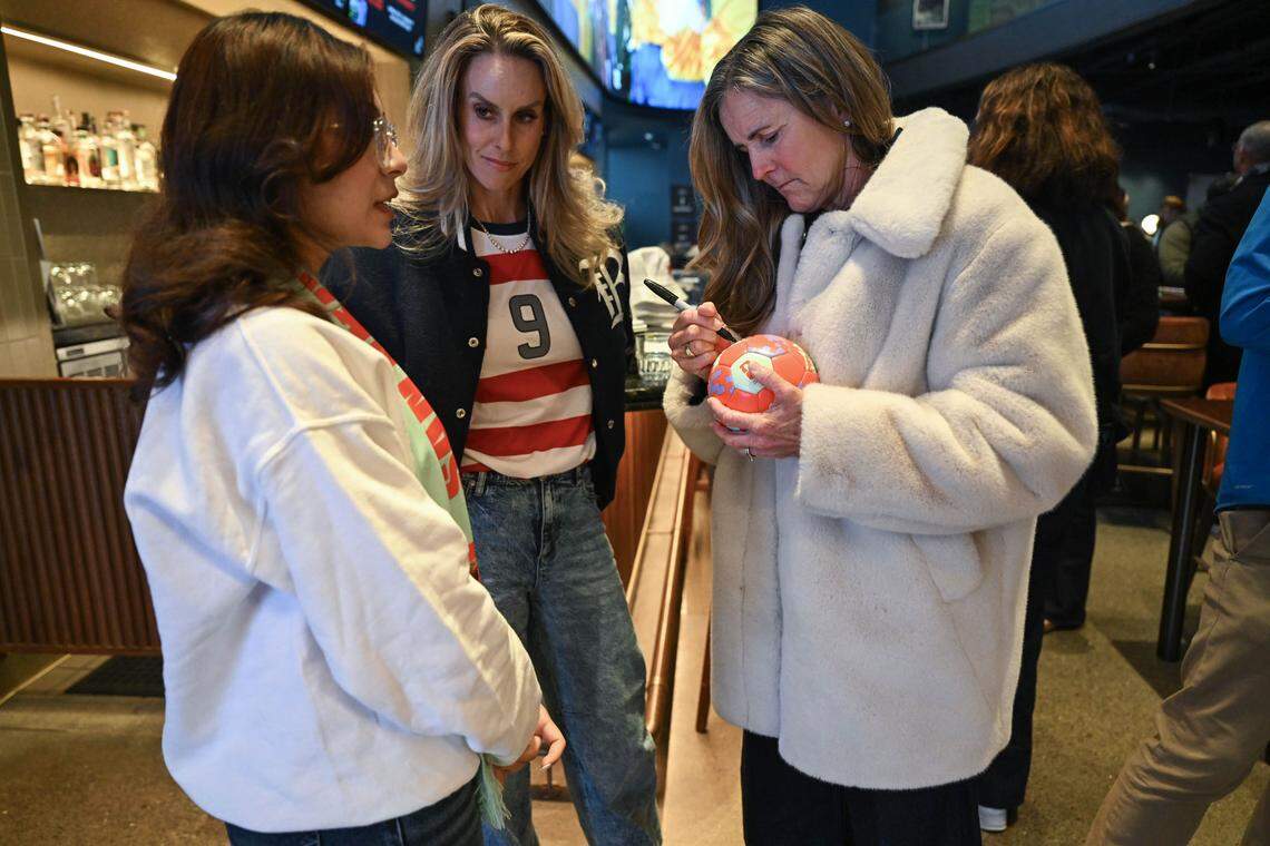 Ruby Delgado, a la izquierda, de San Pablo, tiene un balón firmado por la bicampeona de la FIFA Women’s World Cup Brandi Chastain, mientras posan junto a la exjugadora profesional Leslie Osborne, en el Splash Sports Bar durante el evento del World Cup draw en el Chase Center el viernes.