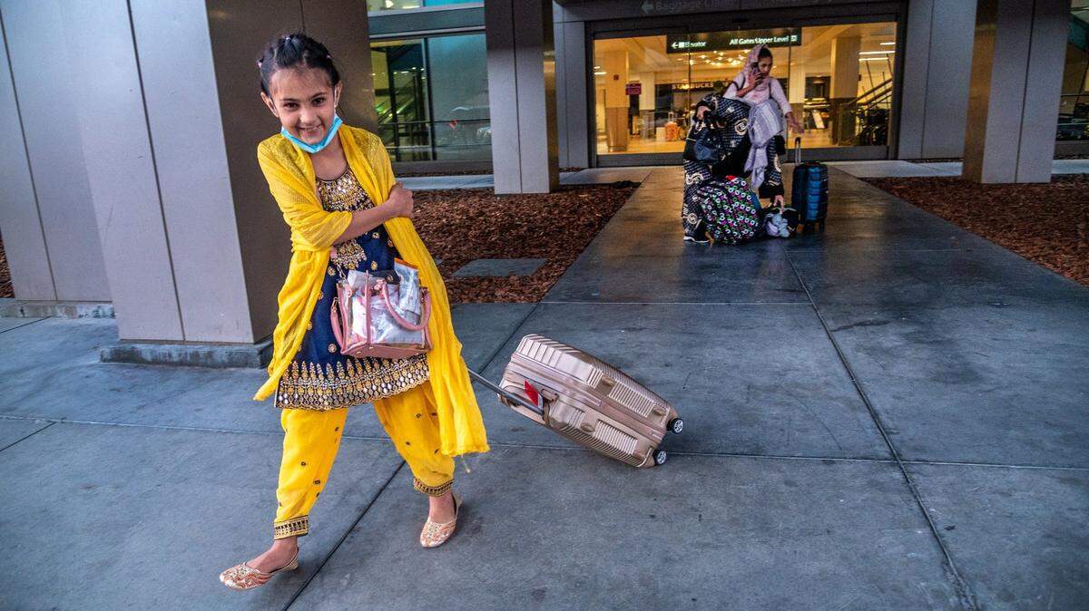 Dyer Kelley Elementary School student Neda, 9, is all smiles as her sister Sabrina, 15, an Encina High School student, watches over their luggage, Monday, Oct. 18, 2021, at the Sacramento International Airport. They returned home to Sacramento with their mother and older sister, after escaping Taliban rule in Afghanistan. They traveled to Afghanistan with their father, who was an Afghan Special Immigrant Visa holder who had settled in Sacramento. While they were there, he died of cancer.
