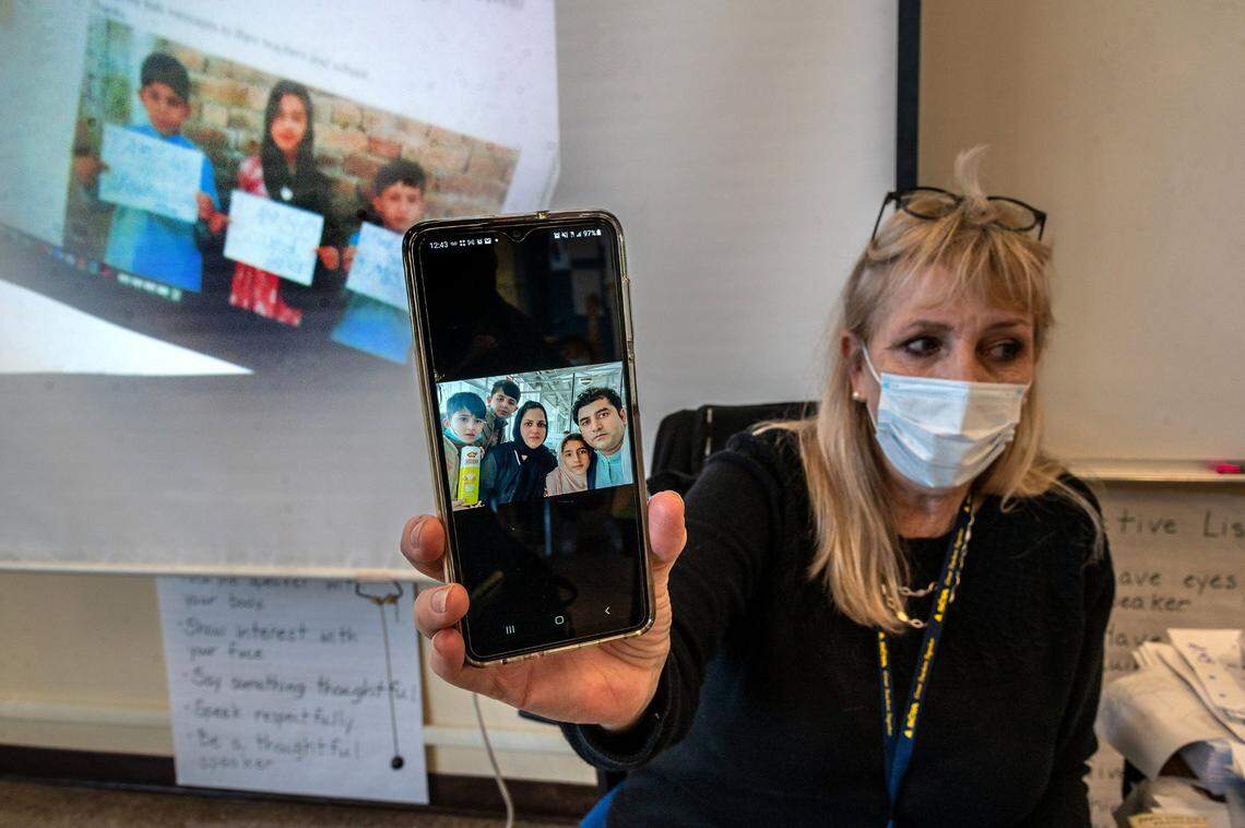 Third grade teacher Jennifer Dare Sparks of Ethel I. Baker Elementary School holds a picture on Oct. 22 that includes the parents of three Afghan students who attend the school as she explains they are safe in the United Arab Emirates. An earlier picture of the children from when they were in hiding from the Taliban is projected on a screen behind her. “We are so looking forward to welcoming them home,” she says.