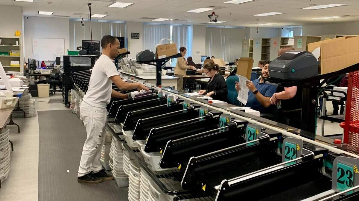 A man sorts a pile of ballots through a large filing machine.
