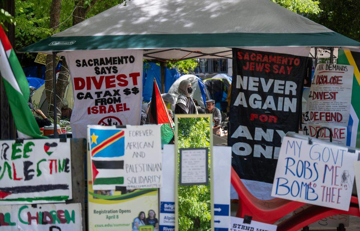 Pro-Palestinian activists walk through a tent opening surrounded by posters on Wednesday, May 1, 2024, at Sacramento State to protest the war in Gaza. The protesters are asking the university to divest from investments in Israel.