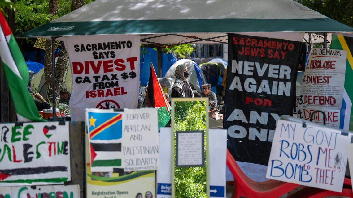 Pro-Palestinian activists walk through a tent opening surrounded by posters on Wednesday, May 1, 2024, at Sacramento State to protest the war in Gaza. The protesters are asking the university to divest from investments in Israel.
