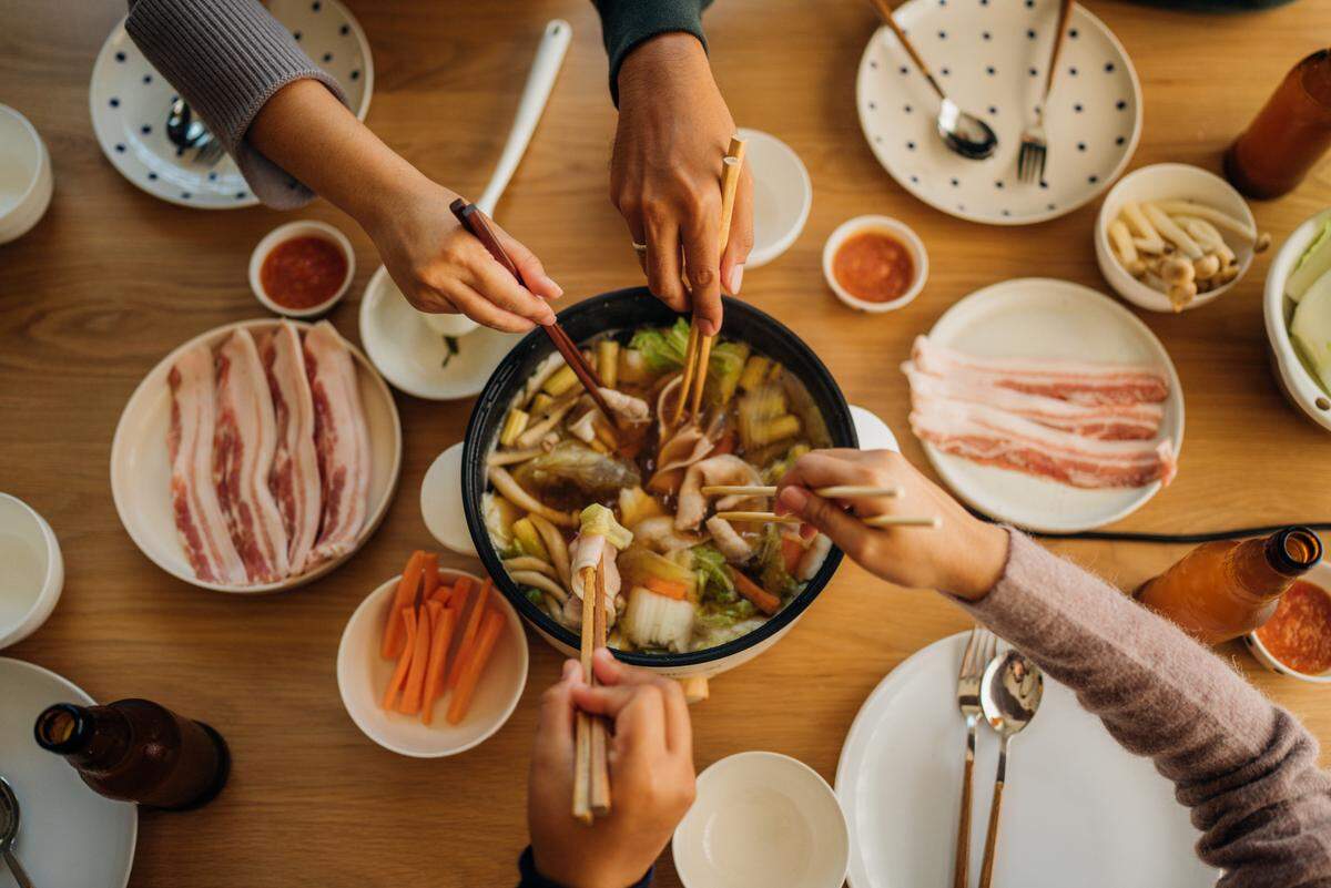Young men and women preparing Japanese hot pot food, or, shabu shabu, with a rice cooker for dinner.