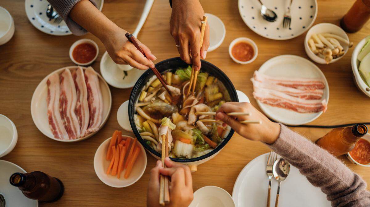 Young men and women preparing Japanese hot pot food, or, shabu shabu, with a rice cooker for dinner.