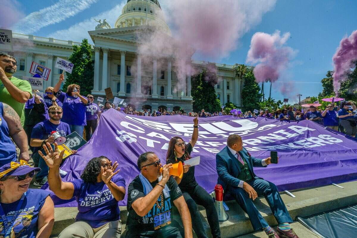 Anica Walls, president of SEIU Local 1000, center, raises her fist during a rally protesting Gov. Gavin Newsom's return-to-office order at the state Capitol on Wednesday. Purple smoke billows behind them as part of the rally.