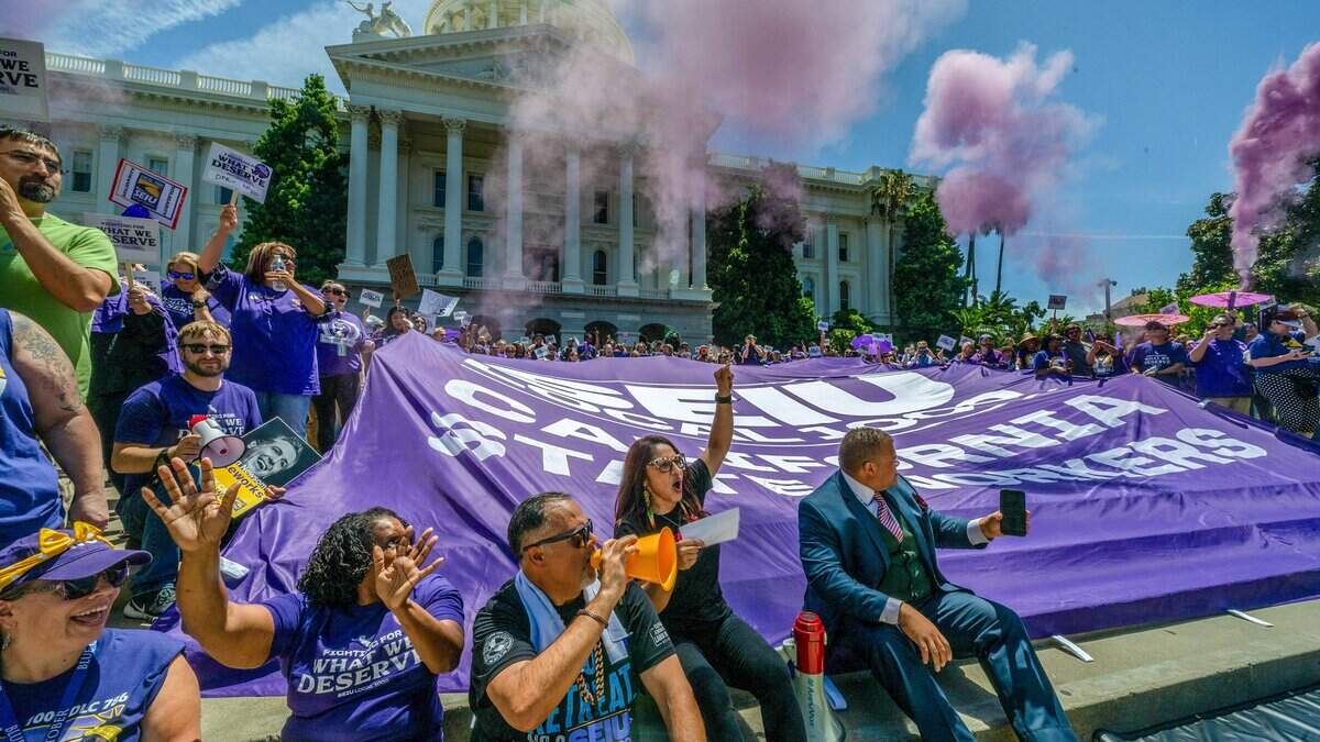 Anica Walls, president of SEIU Local 1000, center, raises her fist during a rally protesting Gov. Gavin Newsom's return-to-office order at the state Capitol on Wednesday, July 1, 2026. Purple smoke billows behind them as part of the rally.