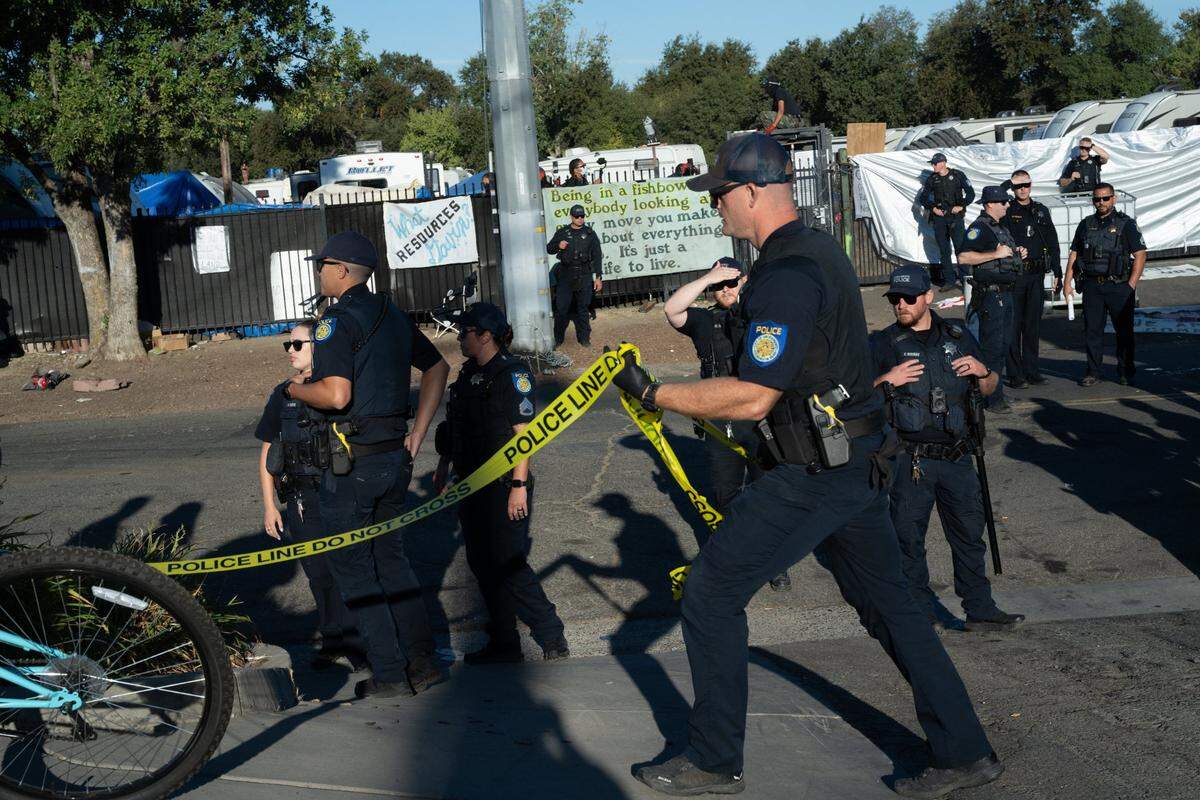 Police move crime scene tape to push media down Arden Way or in an alley beyond where trucks came to tow vehicles during a city sweep of the Camp Resolution homeless encampment Monday.