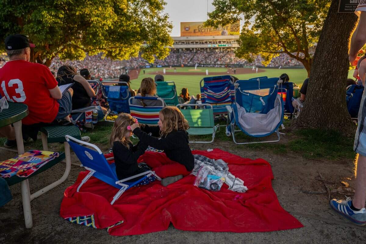 Charlotte, 4, left, and Maddison, 9, adjust each other’s hair and makeup on the right field lawn during a baseball game between the San Francisco Giants and the Athletics at Sutter Health Park on July 4.
