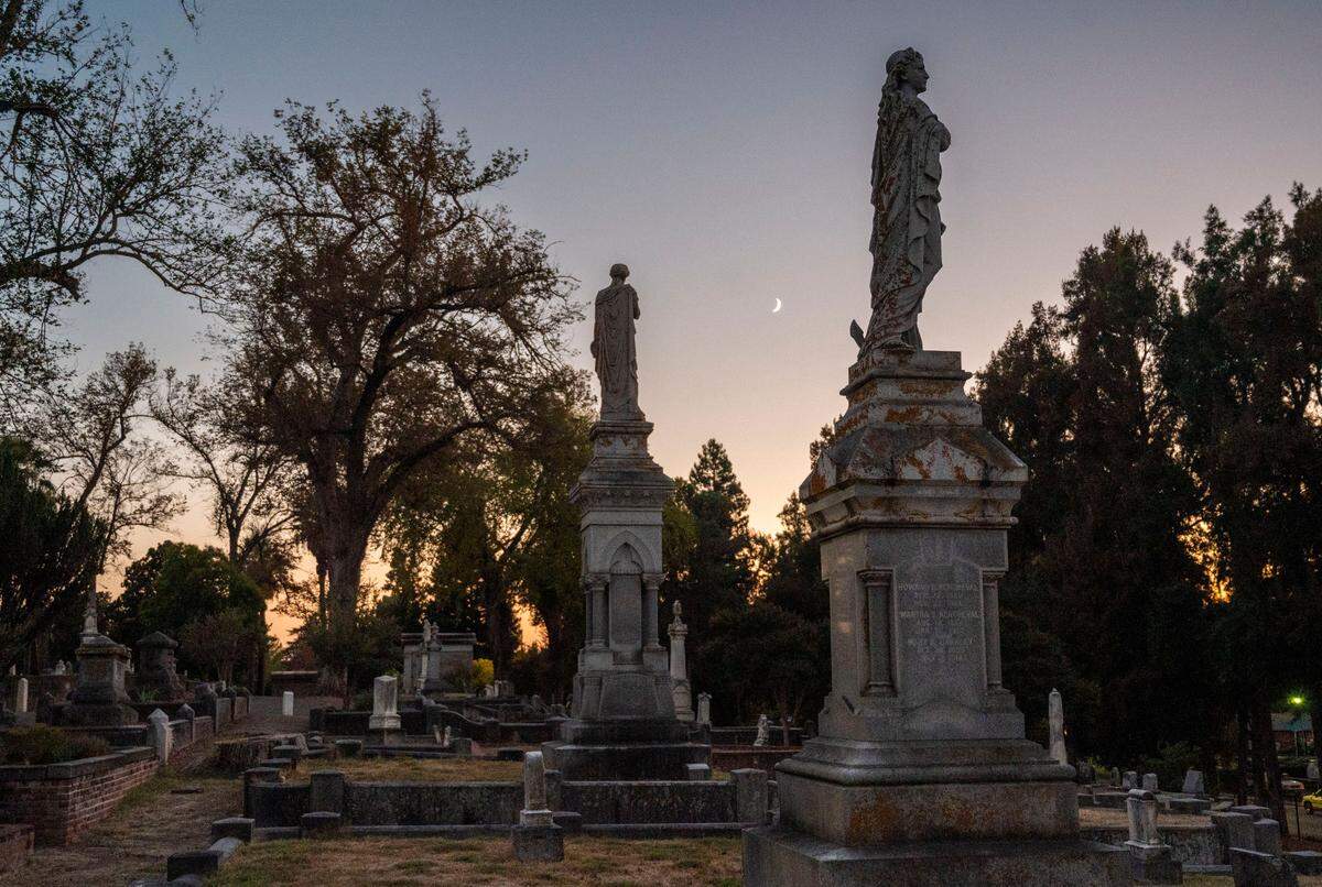 Statue monuments stand in family plots under a crescent moon in 2023 at the Old City Cemetery that date to the mid-19th century. The cemetery was added to the National Register of Historic Places in 2014.